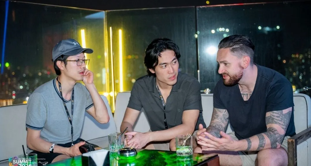 Jake Lam (left) and Phil Chan (center) in conversation with a fellow attendee at a rooftop lounge during SEO Mastery Summit 2026, city skyline at night in the background